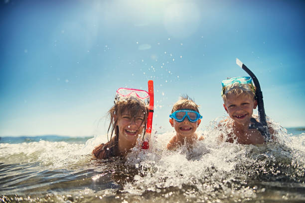 Little boys and their elder sister having fun snorkeling in beautiful sea. The boys aged 8 and girl aged 11 are laughing in warm clear water, wearing diving goggles and snorkel. Sunny summer day.
