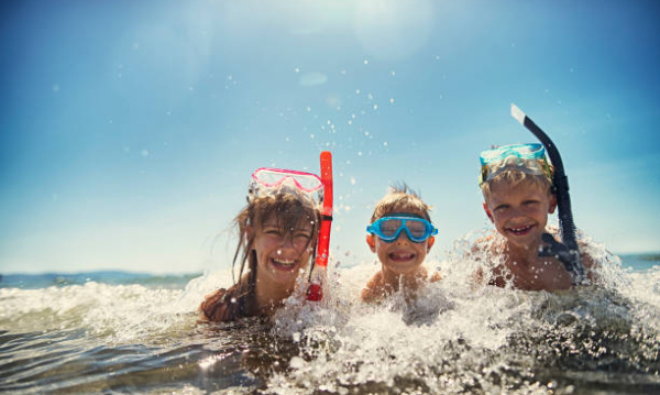 Little boys and their elder sister having fun snorkeling in beautiful sea. The boys aged 8 and girl aged 11 are laughing in warm clear water, wearing diving goggles and snorkel. Sunny summer day.
